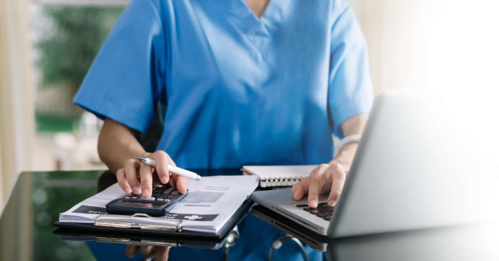 The Growth System Built Specifically for Physical Therapy Clinics 8 - ClickPhys.io Healthcare professional in blue scrubs uses a calculator and laptop at a desk, reviewing documents and notes.